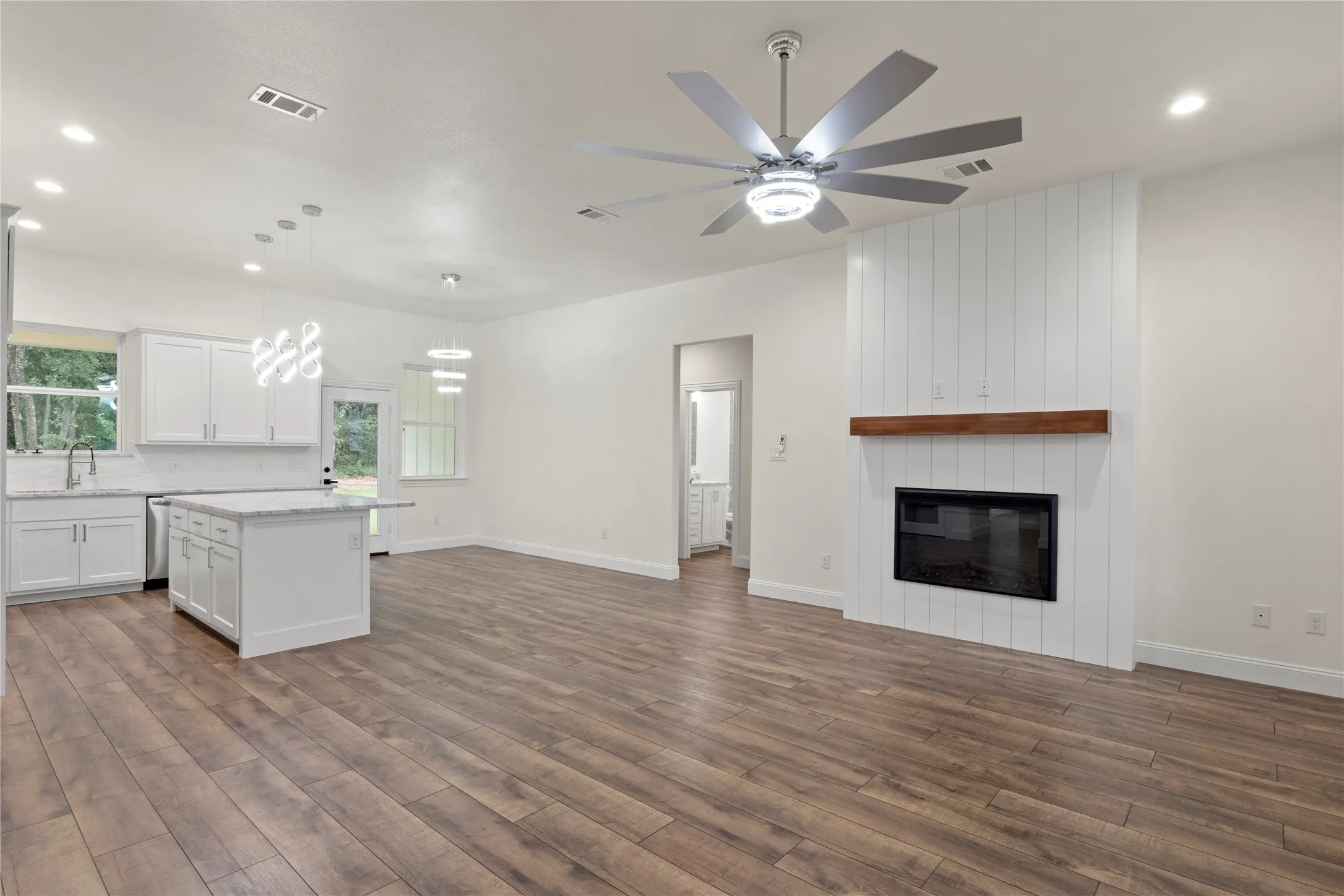 Open-concept living area featuring a fireplace with a wood mantel, wood-finish flooring, and a modern ceiling fan