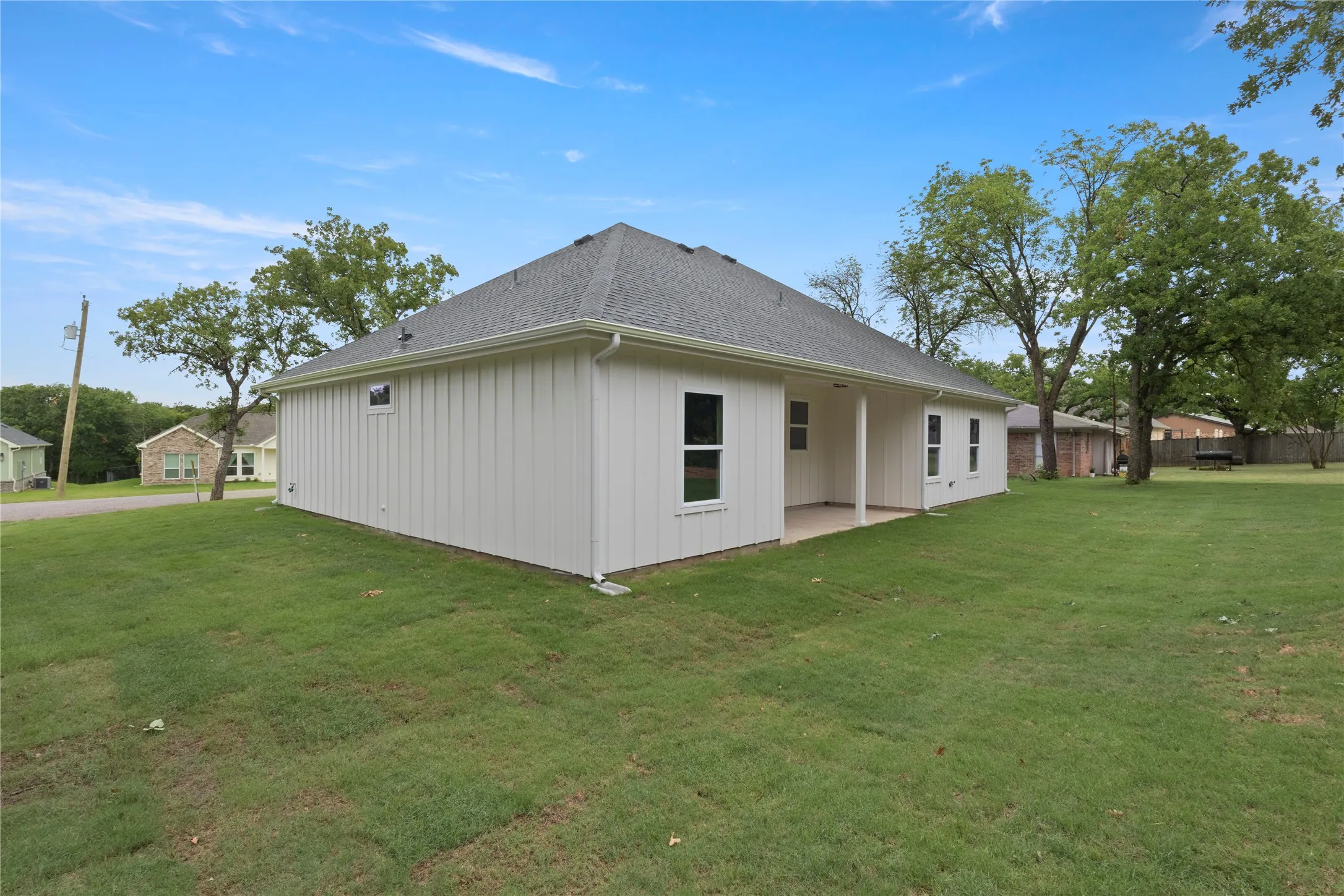Rear exterior featuring white vertical siding, a covered patio, a dark shingle roof, and a spacious lawn