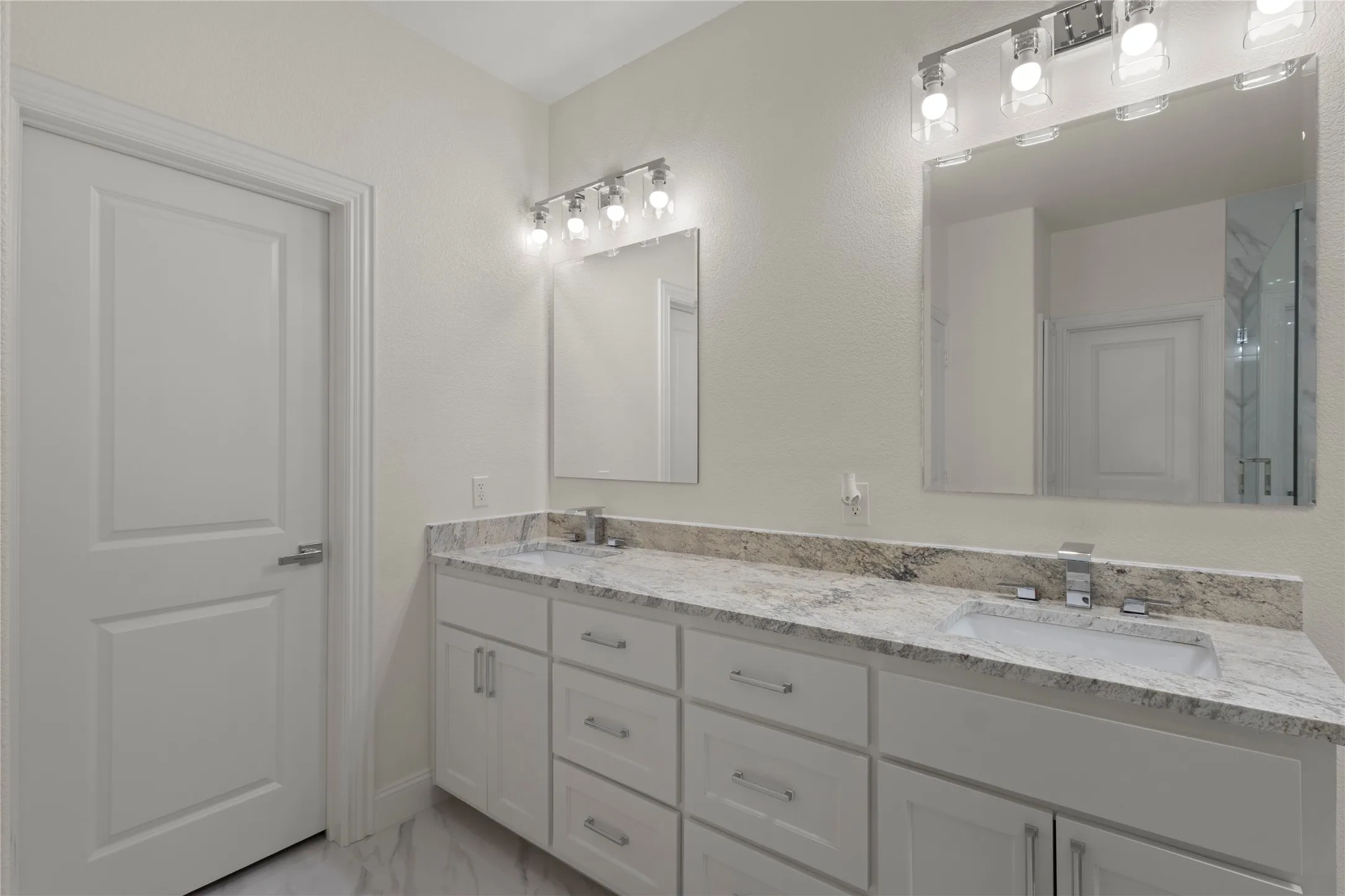 Double vanity featuring white cabinetry, integrated sinks, chrome fixtures, and a light-toned stone countertop