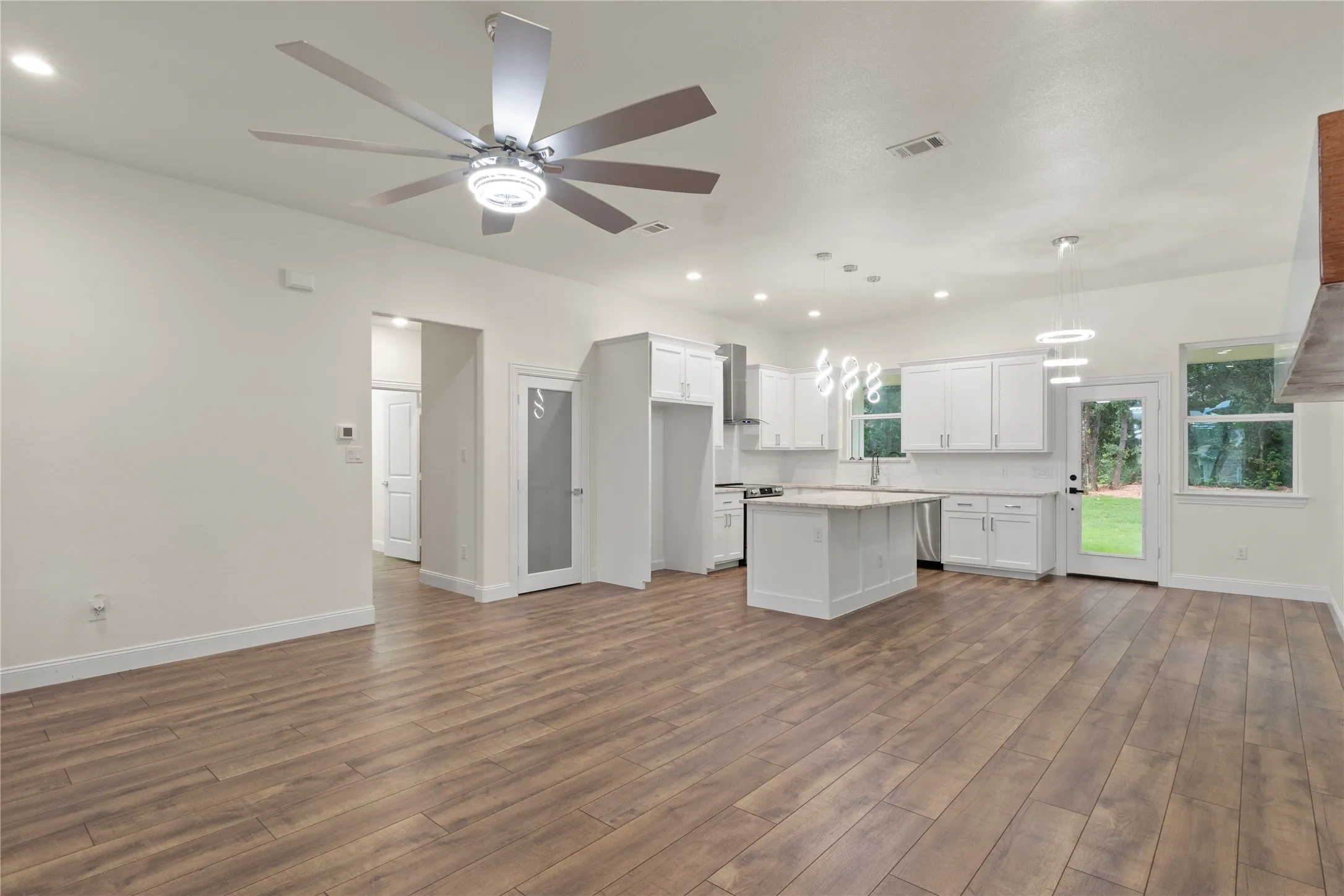 Spacious open-concept living area featuring wood-finish flooring, recessed lighting, and a modern ceiling fan