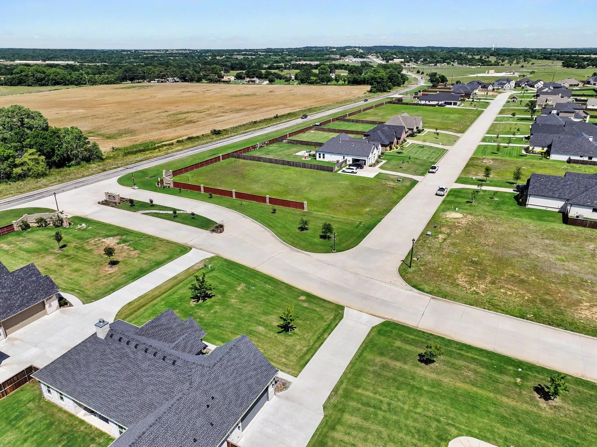 Expansive residential community featuring newly constructed homes with dark shingle roofs, individual concrete driveways, and manicured green lawns