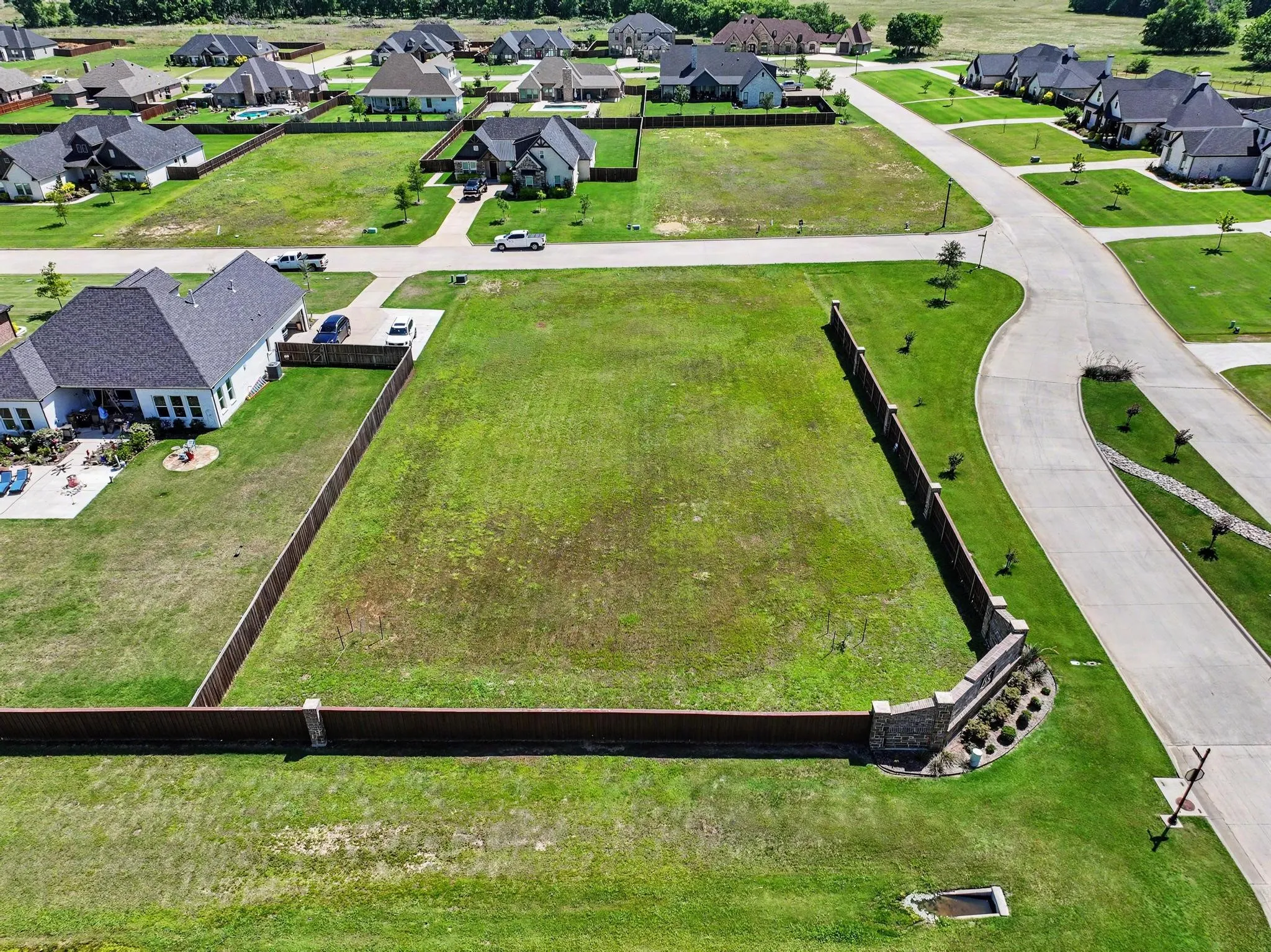 Expansive rectangular lot featuring established perimeter fencing and a decorative stone and shrub border along the street frontage