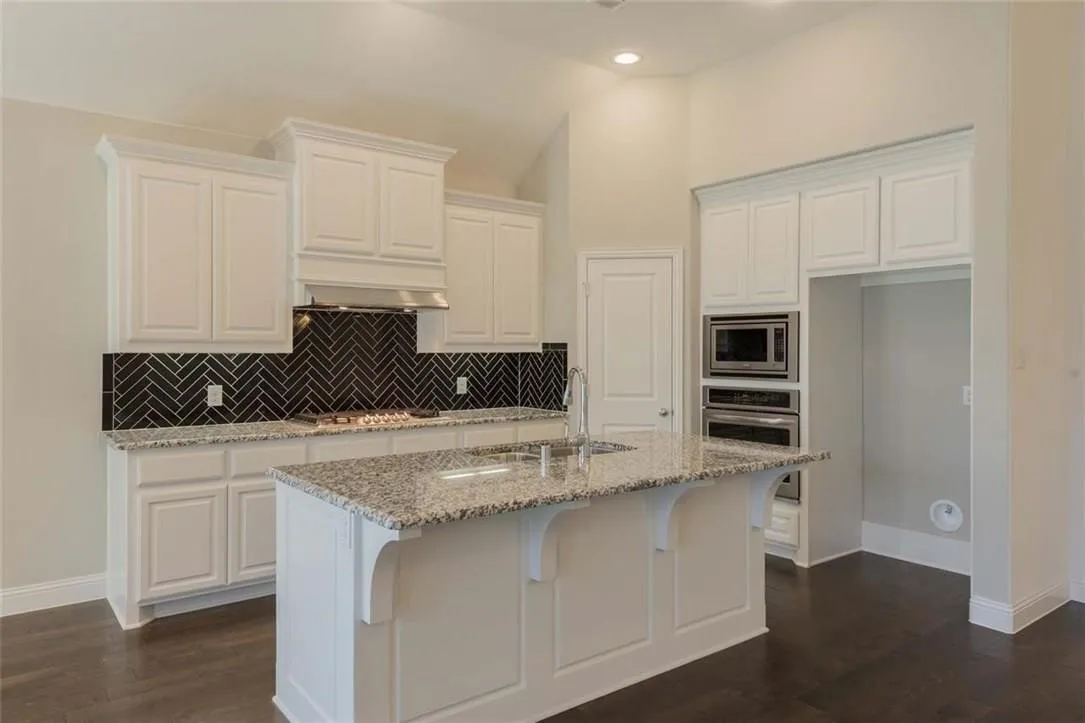 Kitchen featuring white cabinetry, a central island with a light-toned countertop, a herringbone pattern backsplash, and stainless steel built-in appliances