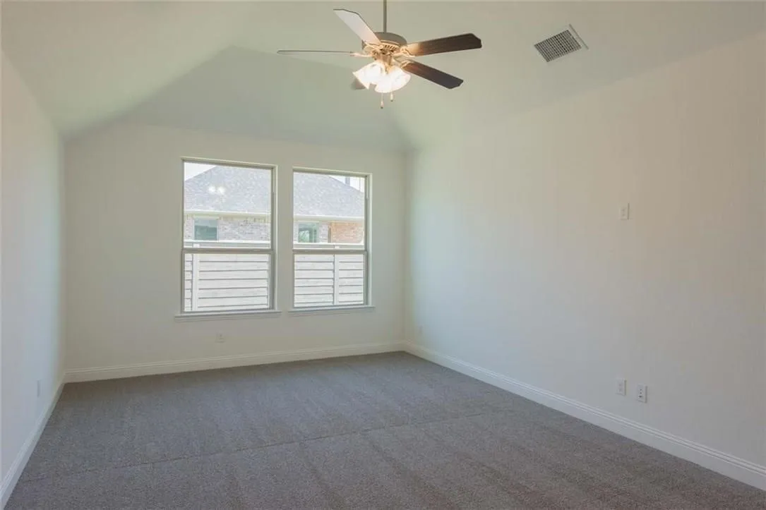 Vaulted ceiling room featuring two windows with horizontal blinds, a ceiling fan with integrated lighting, and gray carpeting