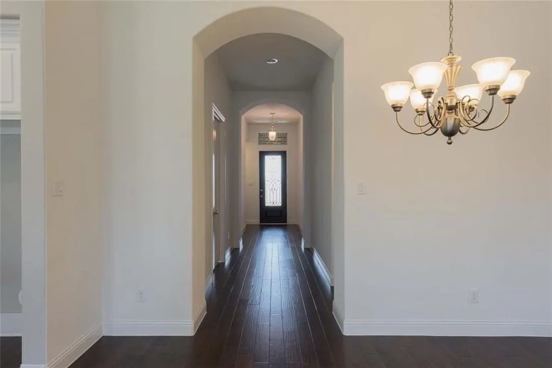 Long foyer featuring wood-finish flooring, an arched entryway, and white baseboards