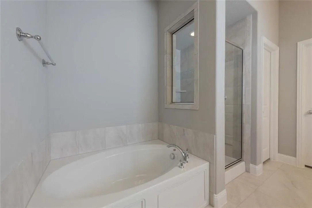 Soaking tub with tile surround, chrome fixtures, and a window