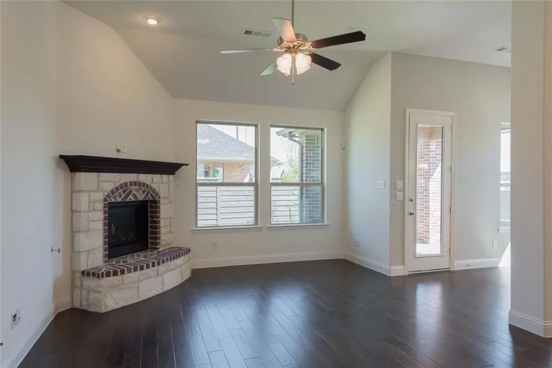 Vaulted ceiling living area featuring a stone and brick fireplace with a dark wood mantel, rich wood-finish flooring, recessed lighting, and a ceiling fan