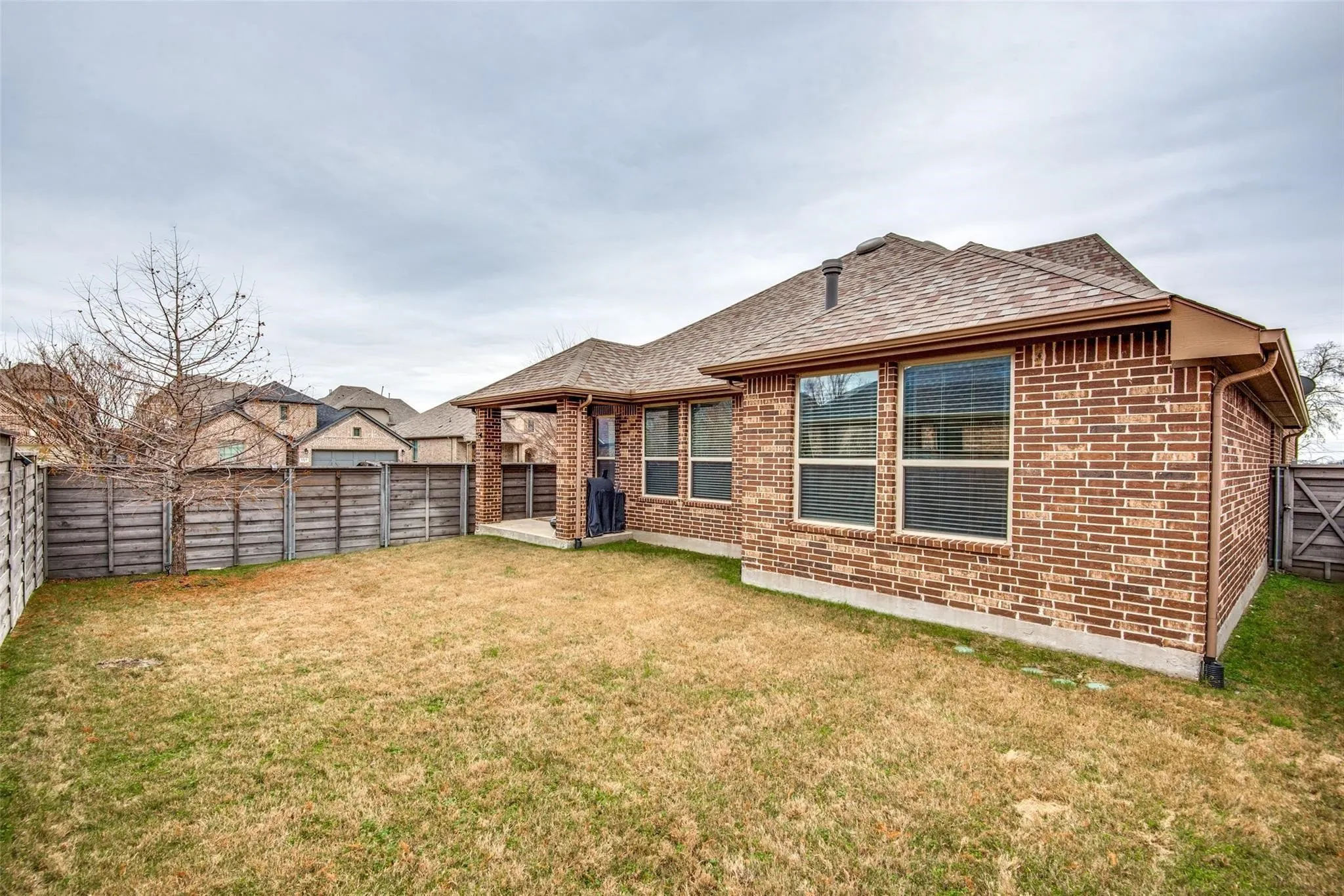 Expansive backyard featuring a manicured lawn, full privacy fencing, and a covered patio area
