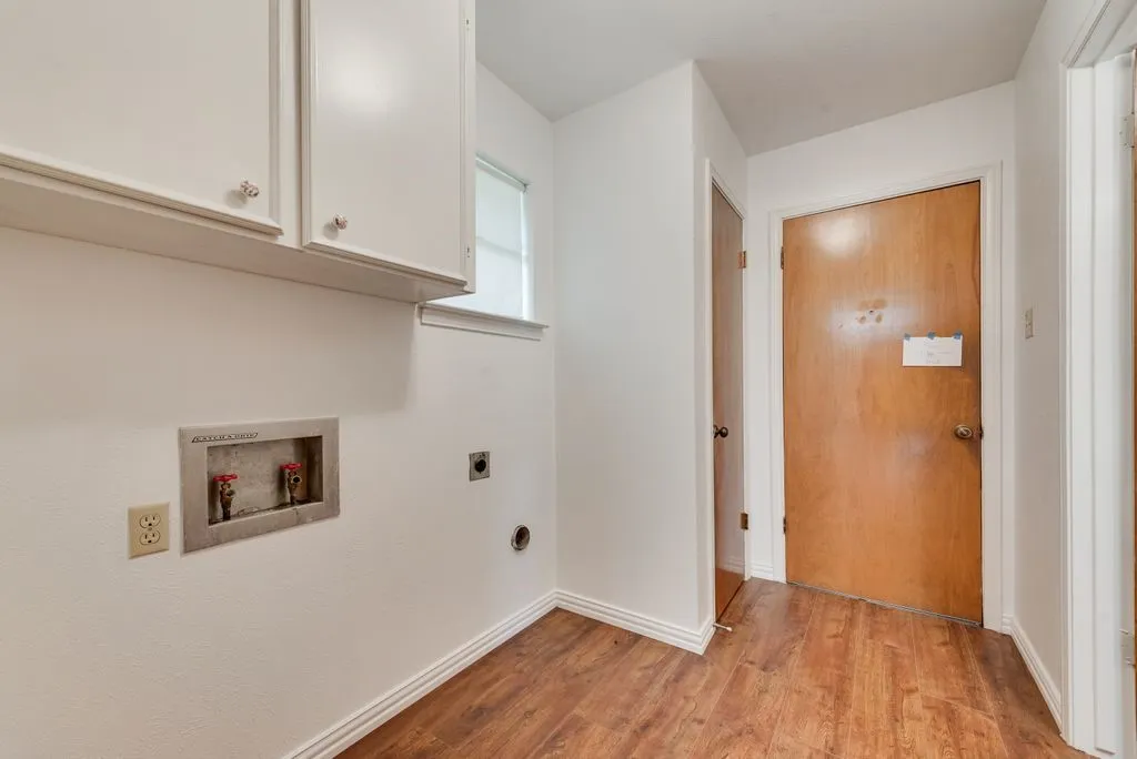 Laundry area featuring wood-finish flooring and white cabinetry