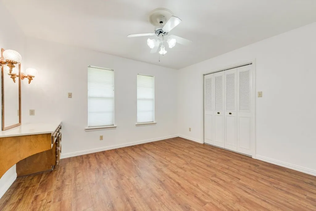 Spacious room with wood-finish flooring, two windows, and a ceiling fan with integrated lighting