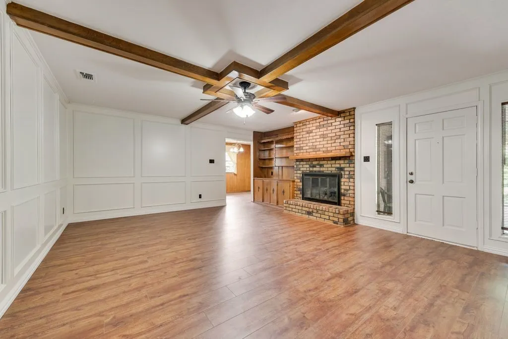 Spacious room featuring wood-finish flooring, white paneled walls, and a ceiling fan