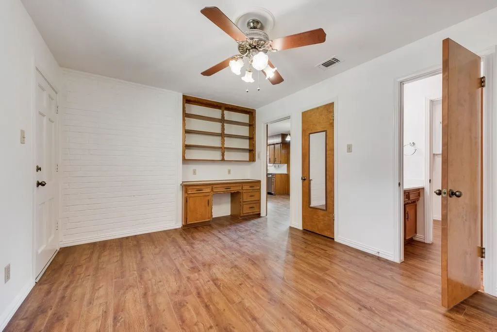 Room featuring wood-finish flooring, a ceiling fan, and a built-in wood desk with shelving
