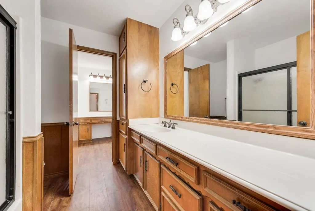 Bathroom vanity featuring a single sink, an expansive mirror, and a wood-finish cabinet with multiple storage compartments