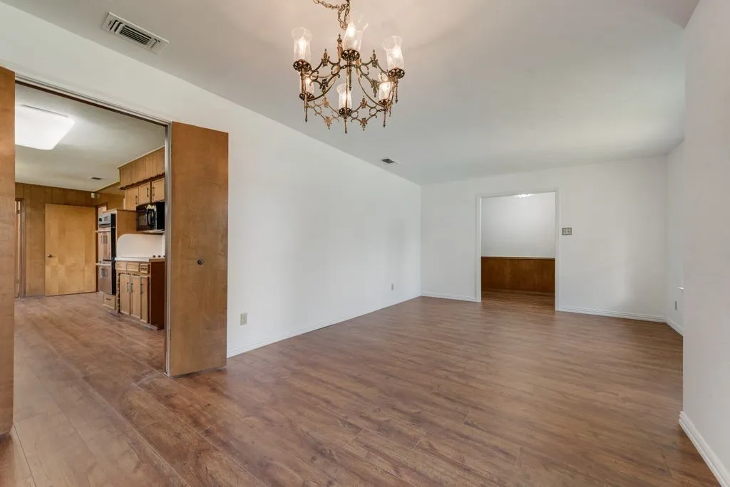 Expansive room featuring wood-finish flooring, white walls, and a decorative chandelier