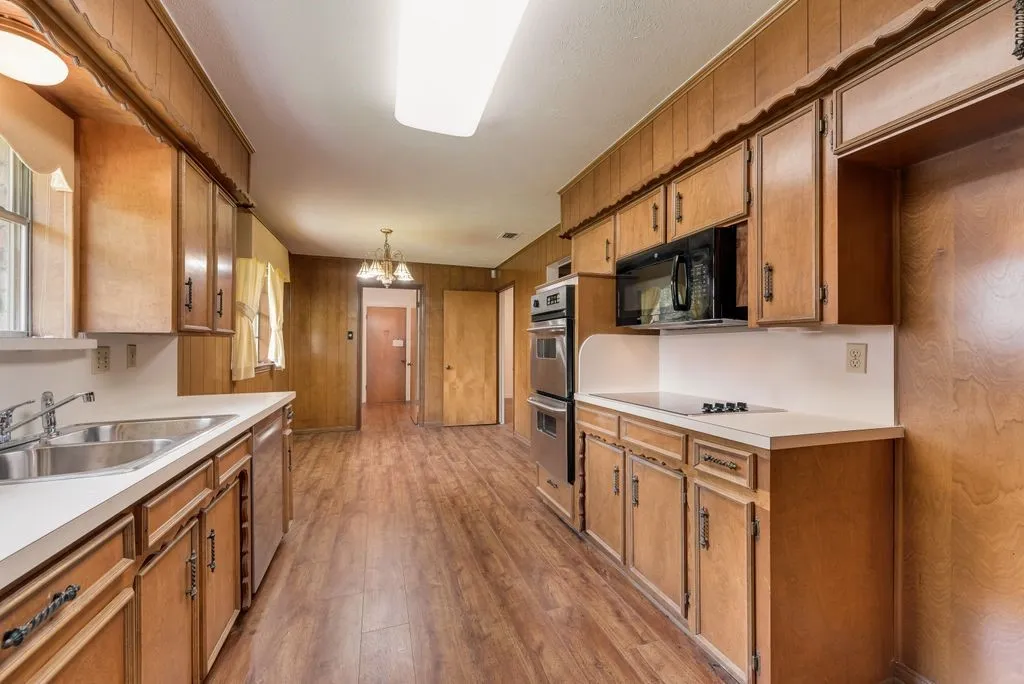 Kitchen featuring wood-finish flooring, wood paneling, extensive cabinetry, double wall ovens, and a built-in microwave