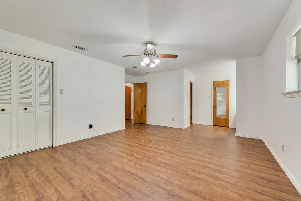 Spacious room featuring wood-finish flooring, white walls, and a ceiling fan with integrated lighting