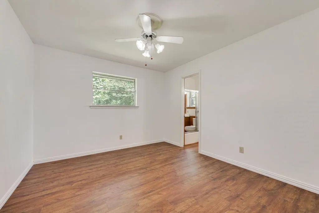 Spacious room featuring wood-finish flooring, white baseboards, a ceiling fan with integrated lighting, and a window providing natural light