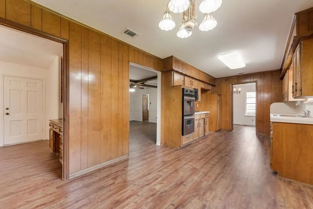 Kitchen featuring wood-finish flooring, wood paneling, wood cabinetry, built-in double ovens, and a dual-basin sink