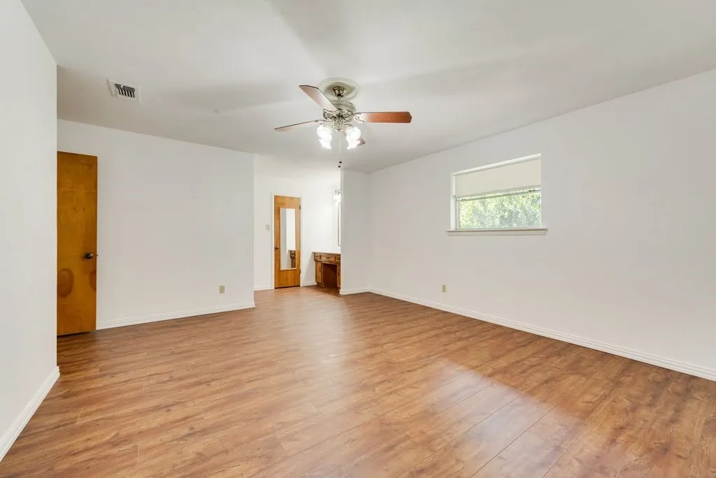 Spacious room featuring wood-finish flooring, white walls, and a ceiling fan with integrated lighting