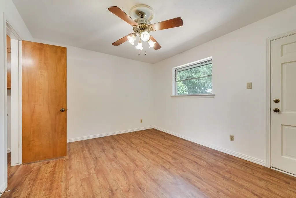 Spacious room featuring wood-finish flooring, a ceiling fan with light fixture, and a window with exterior views