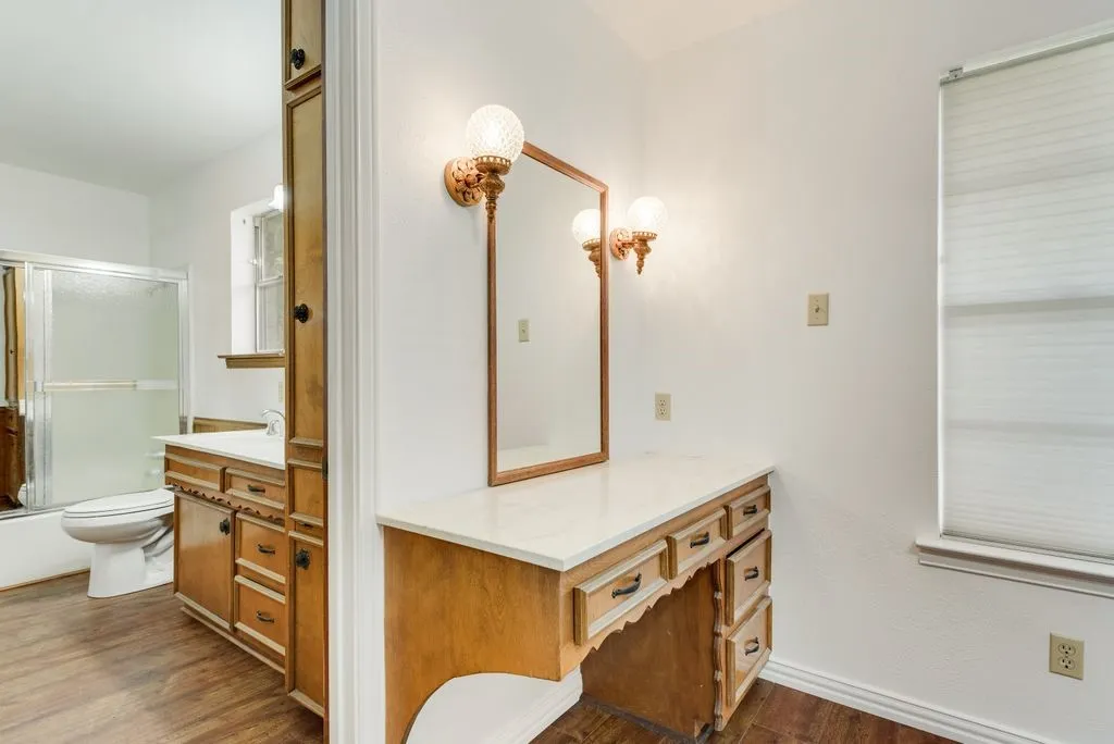 Vanity area featuring a built-in wood-finish desk with a light-toned countertop, a framed mirror, and two decorative wall sconces