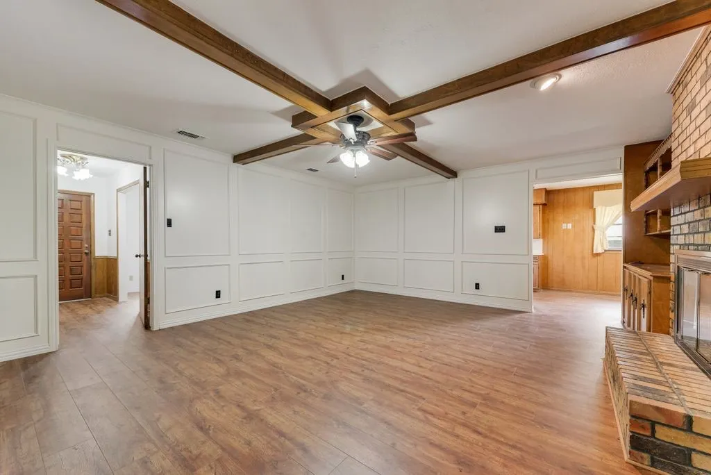 Open-concept living space featuring wood-finish flooring, white wainscoting, and exposed wood ceiling beams with a ceiling fan