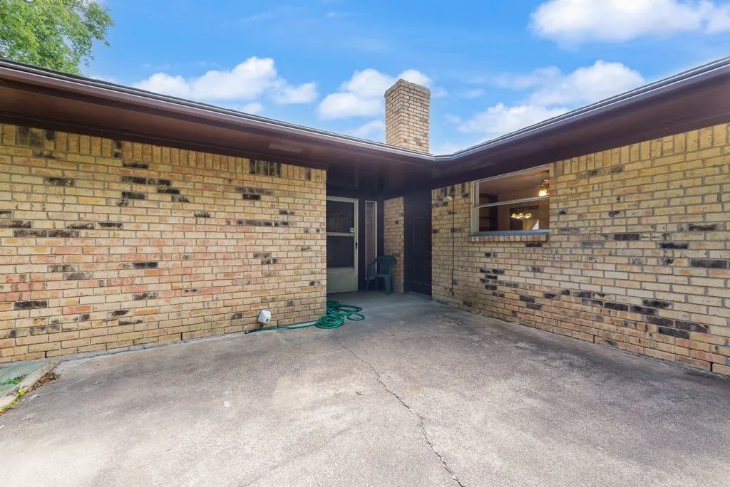 Exterior brick facade featuring a chimney, a window, and a concrete patio