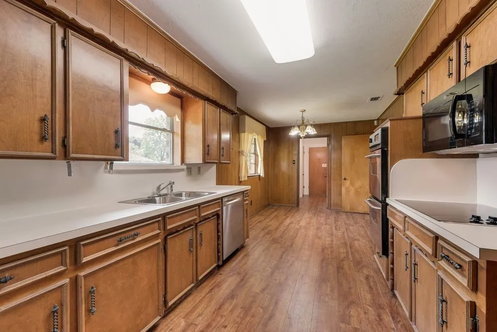 Galley kitchen featuring wood-finish flooring, abundant wood cabinetry, white countertops, and a double basin stainless steel sink