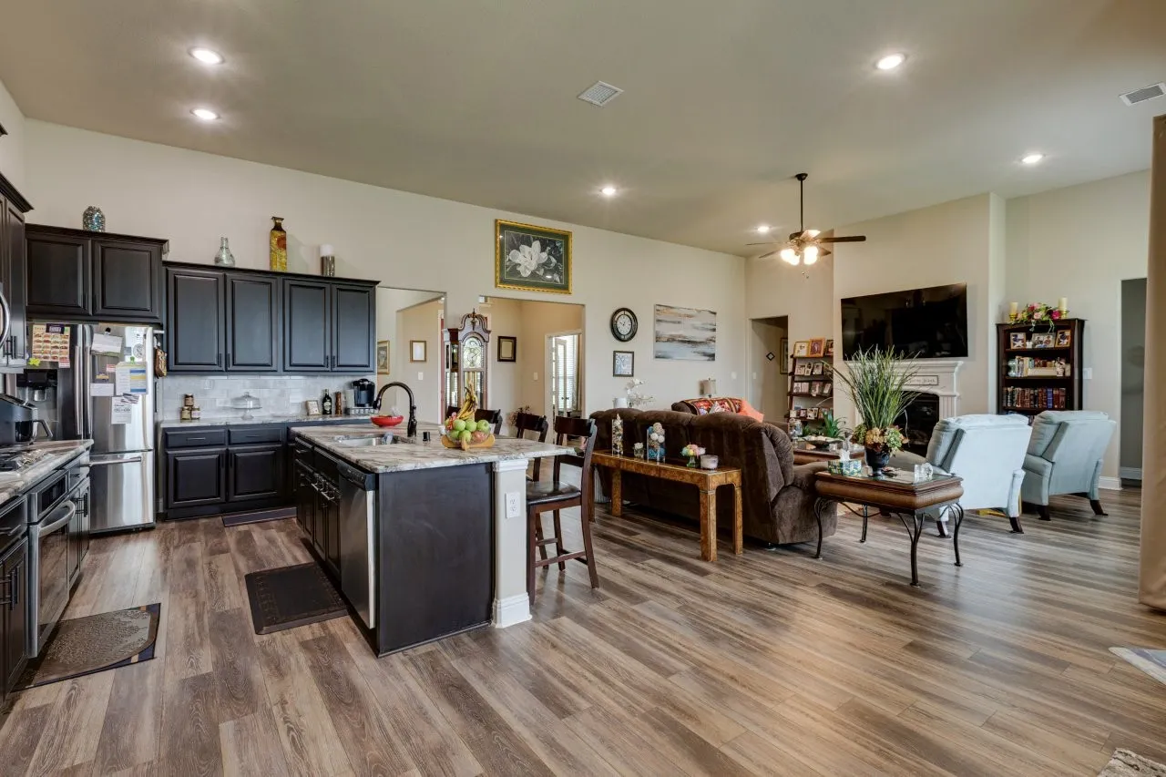 Open-concept living area featuring wood-finish flooring, recessed lighting, and a kitchen with dark cabinetry and stainless-steel appliances