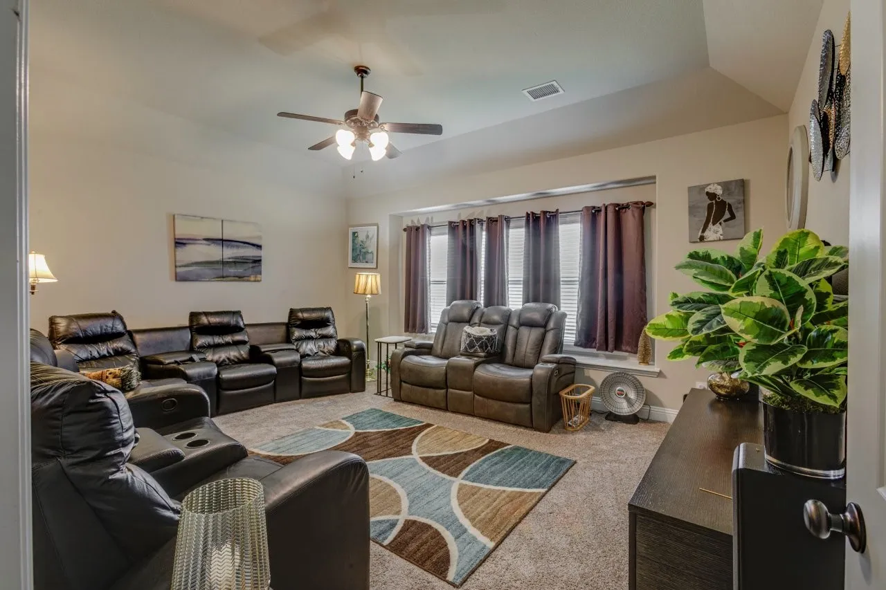 Carpeted living area featuring a vaulted ceiling with a ceiling fan, a bay window with blinds, and neutral wall tones