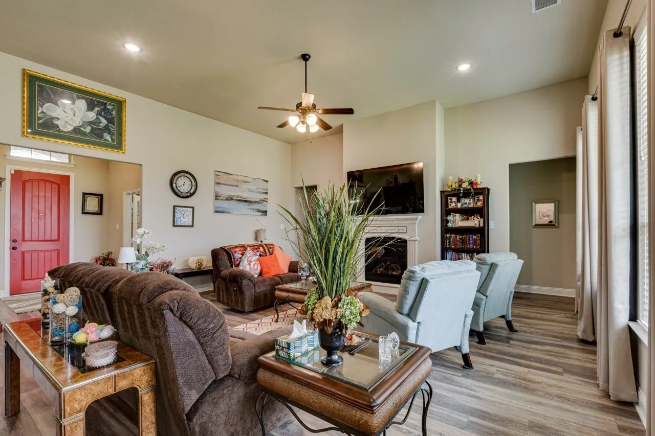 Spacious living area featuring wood-finish flooring, a ceiling fan, recessed lighting, and an elegant fireplace with a mantel