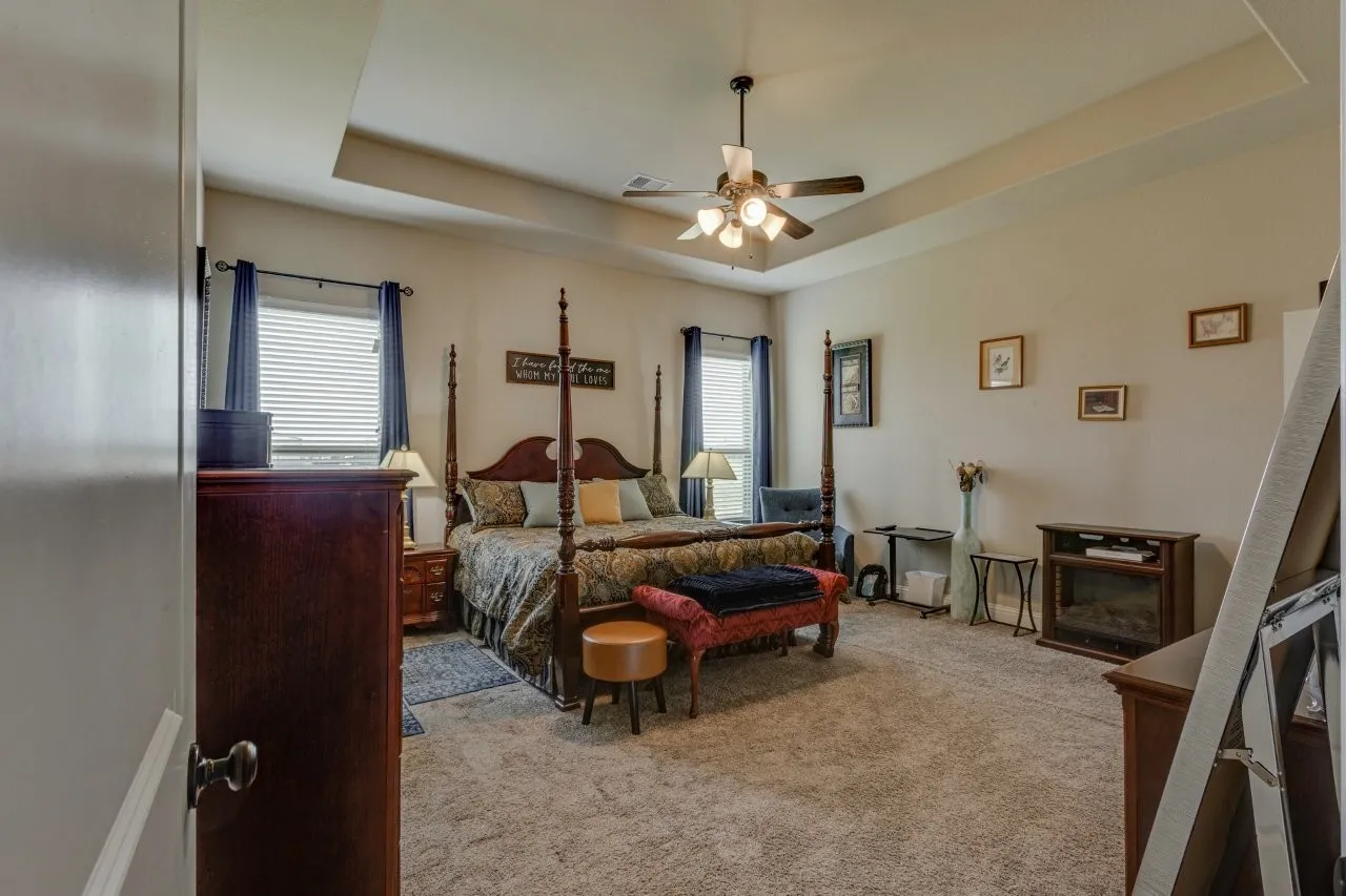 Carpeted room featuring a tray ceiling with a ceiling fan, two windows with blinds, and a built-in media console with an electric fireplace