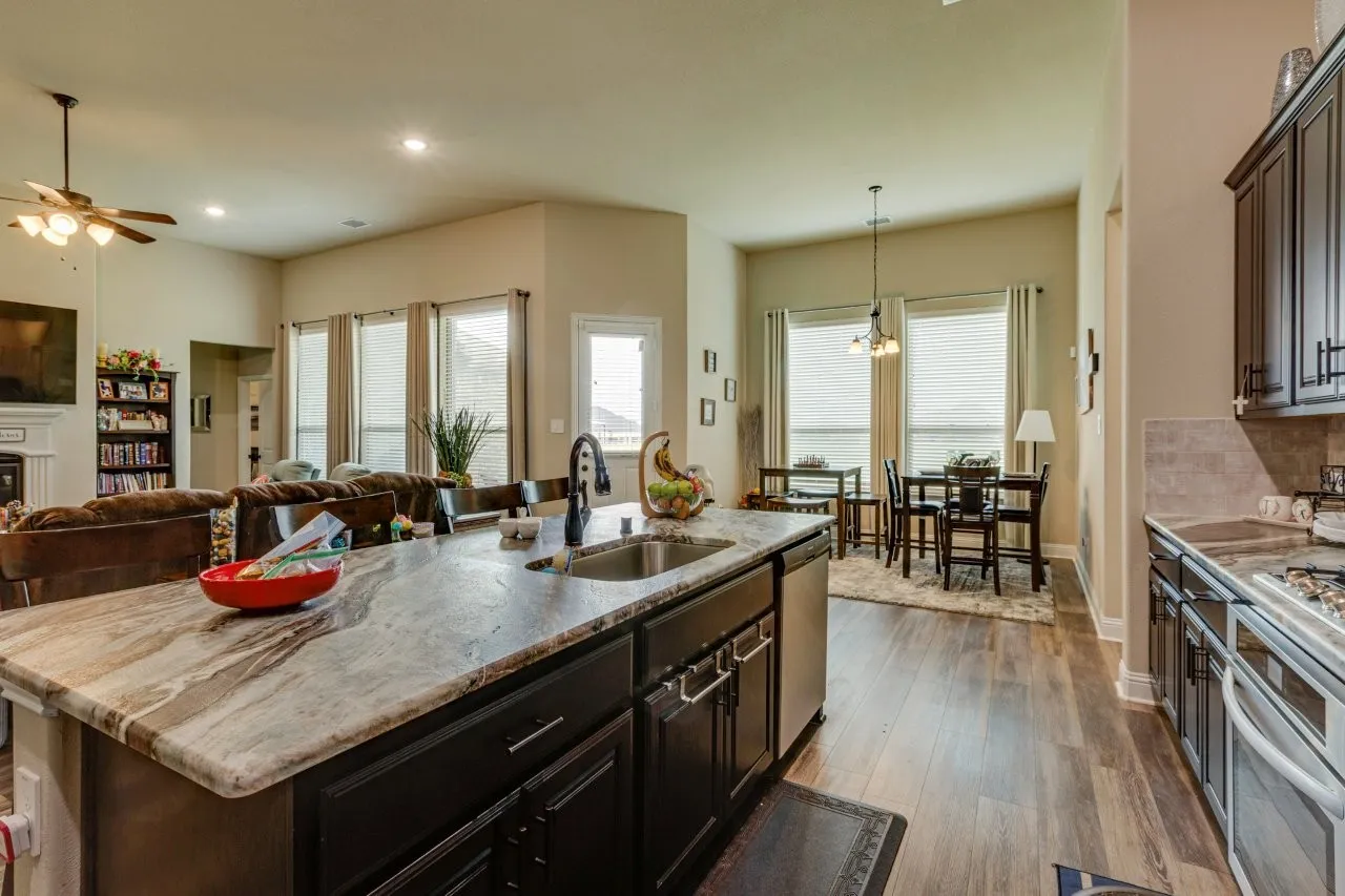 Spacious kitchen island featuring a deep sink and an integrated dishwasher, complemented by dark wood-finish cabinetry and light-toned countertops