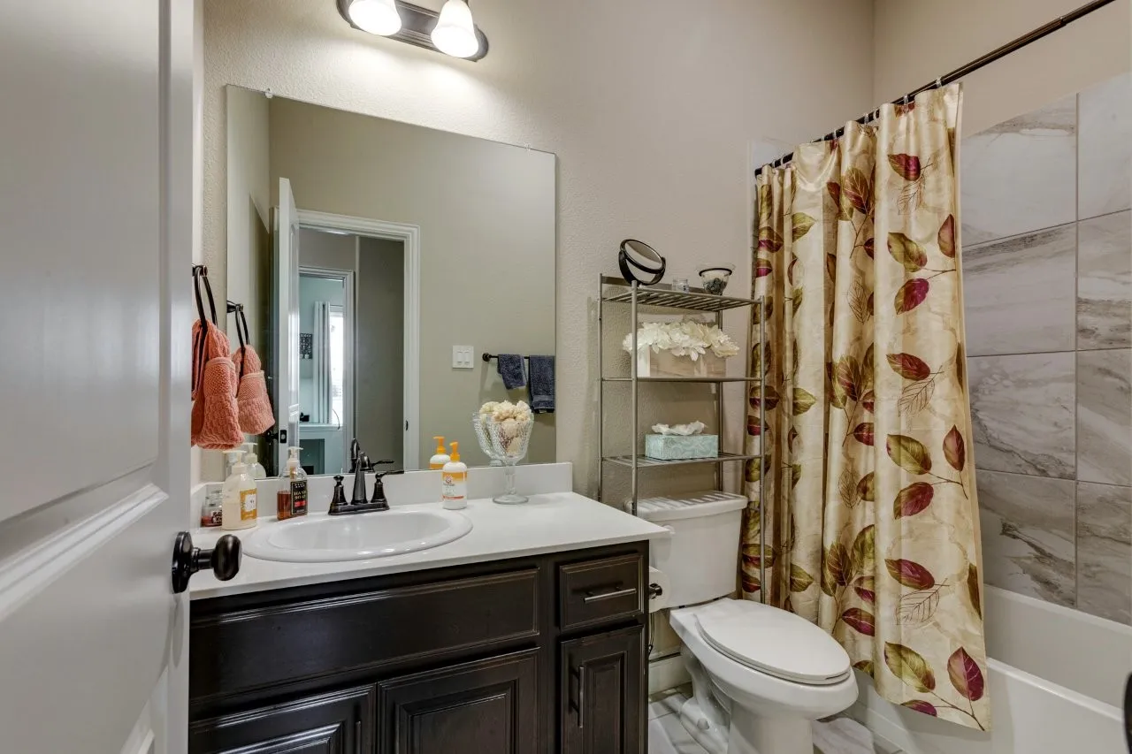 Bathroom featuring a dark wood vanity with a white countertop and undermount sink, a large wall-mounted mirror, a two-bulb vanity light, and a tiled shower/tub combination