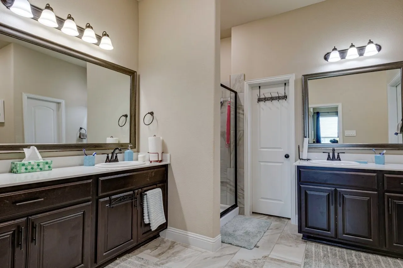 Double vanity featuring dark wood-finish cabinetry, white countertops, and framed mirrors with overhead lighting