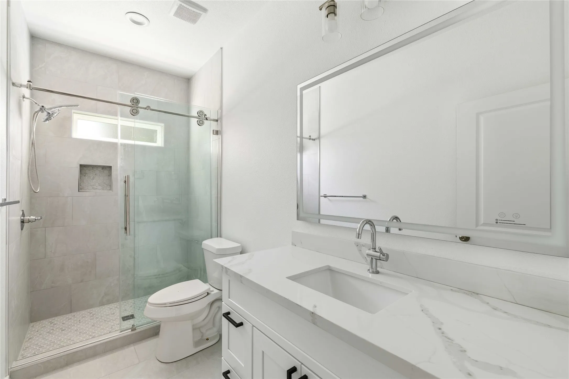 Spa-inspired primary bathroom featuring a frameless glass-enclosed walk-in shower with linear drain and subway tile surround, dual-sink vanity with white quartz countertop and chrome fixtures, large illuminated mirror, and polished tile flooring throughout