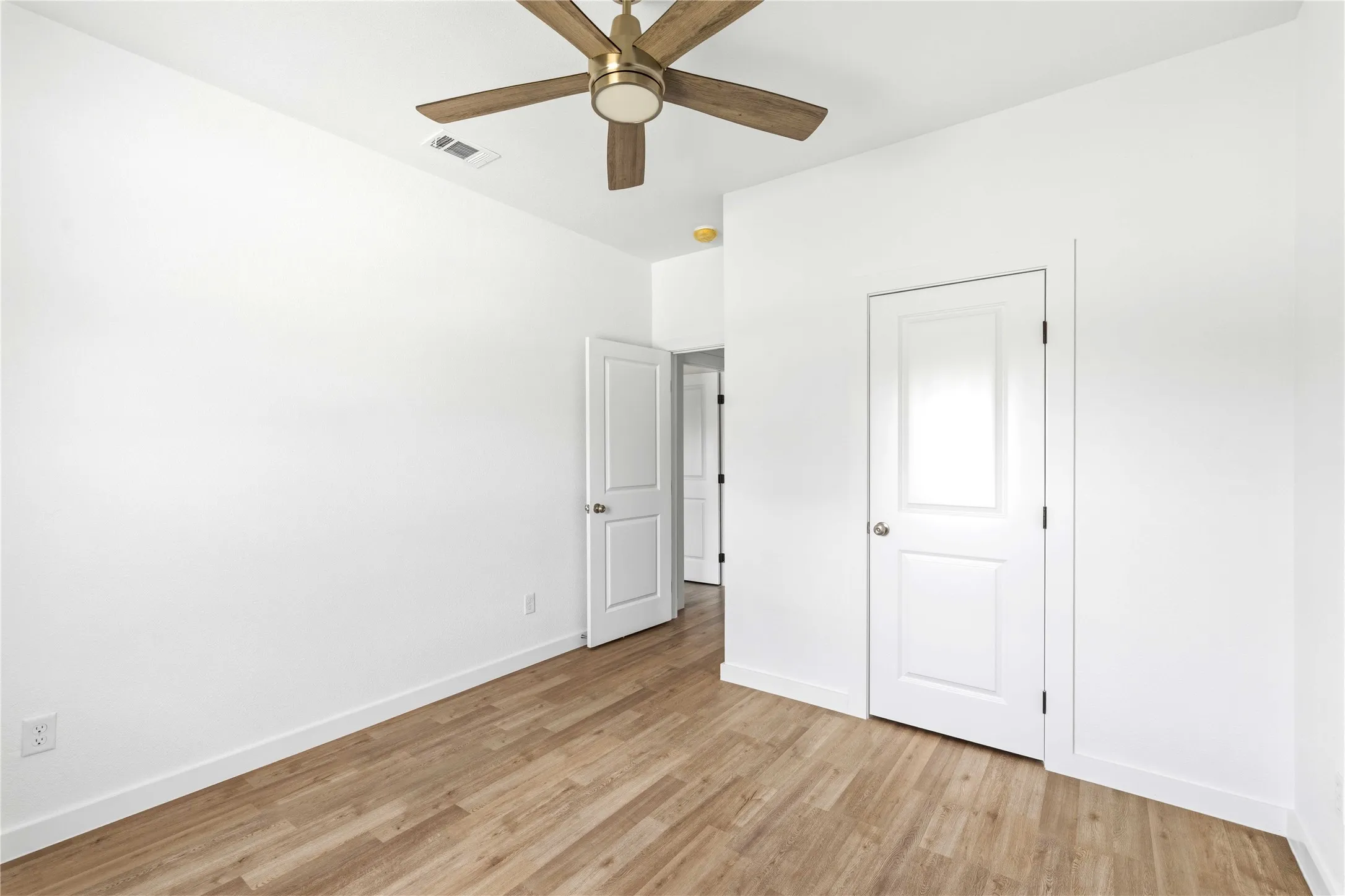 Wood-finish flooring, white walls, and a ceiling fan with gold-tone accents
