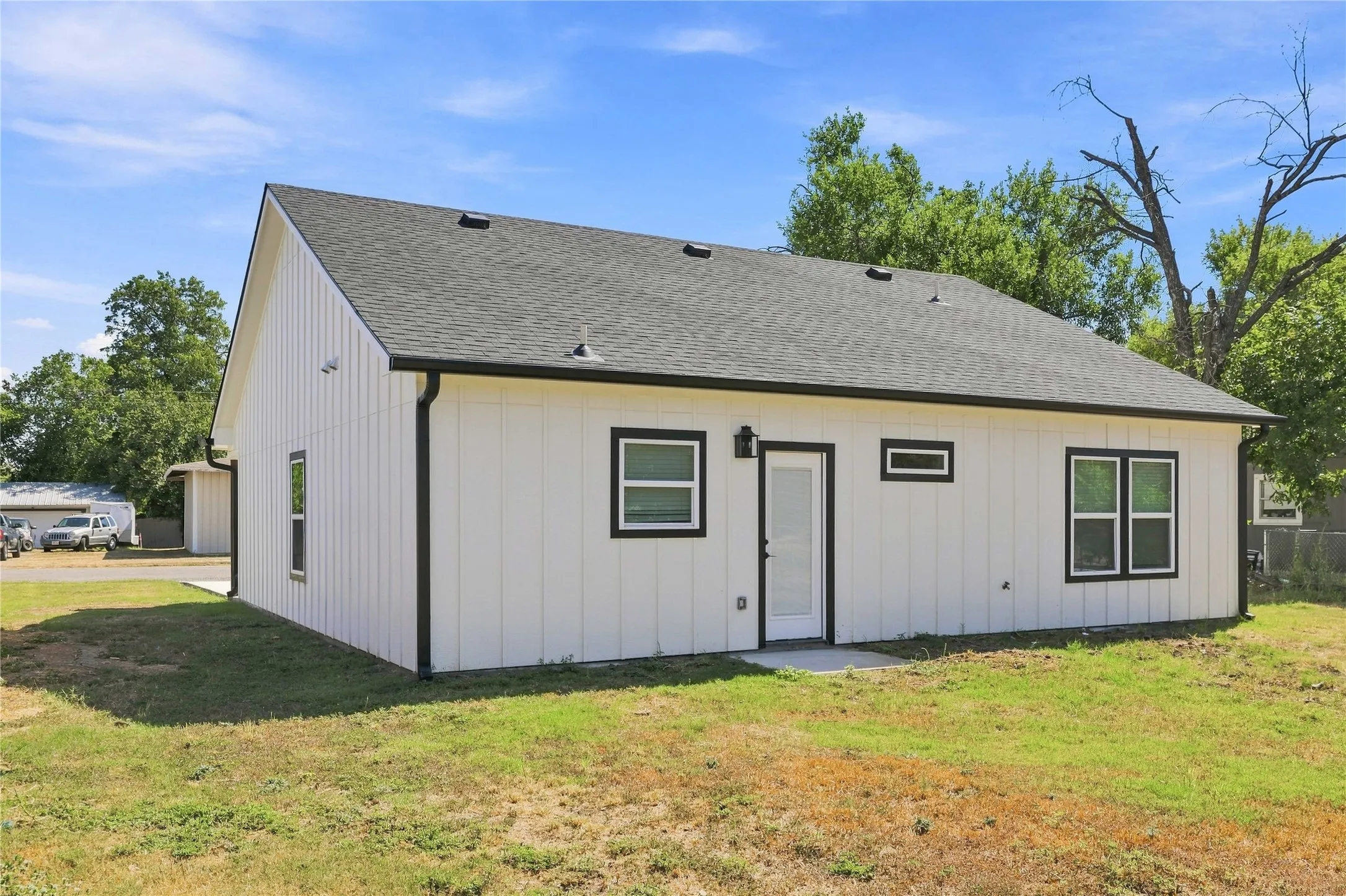 White vertical siding exterior with black trim, black shingle roof, and a rear entry door
