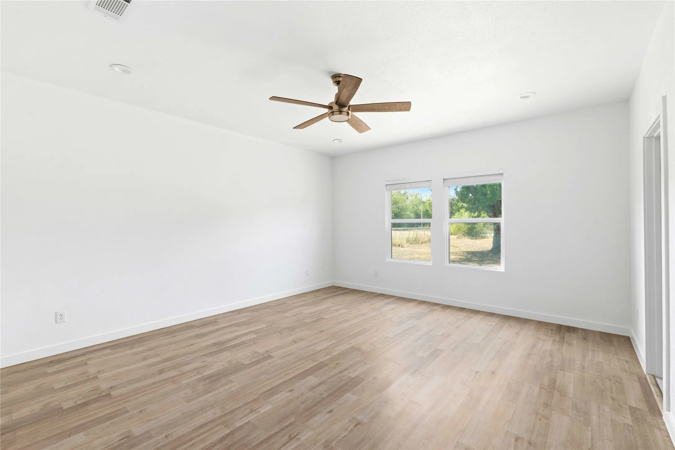 Spacious room featuring light wood-finish flooring, recessed lighting, and a ceiling fan