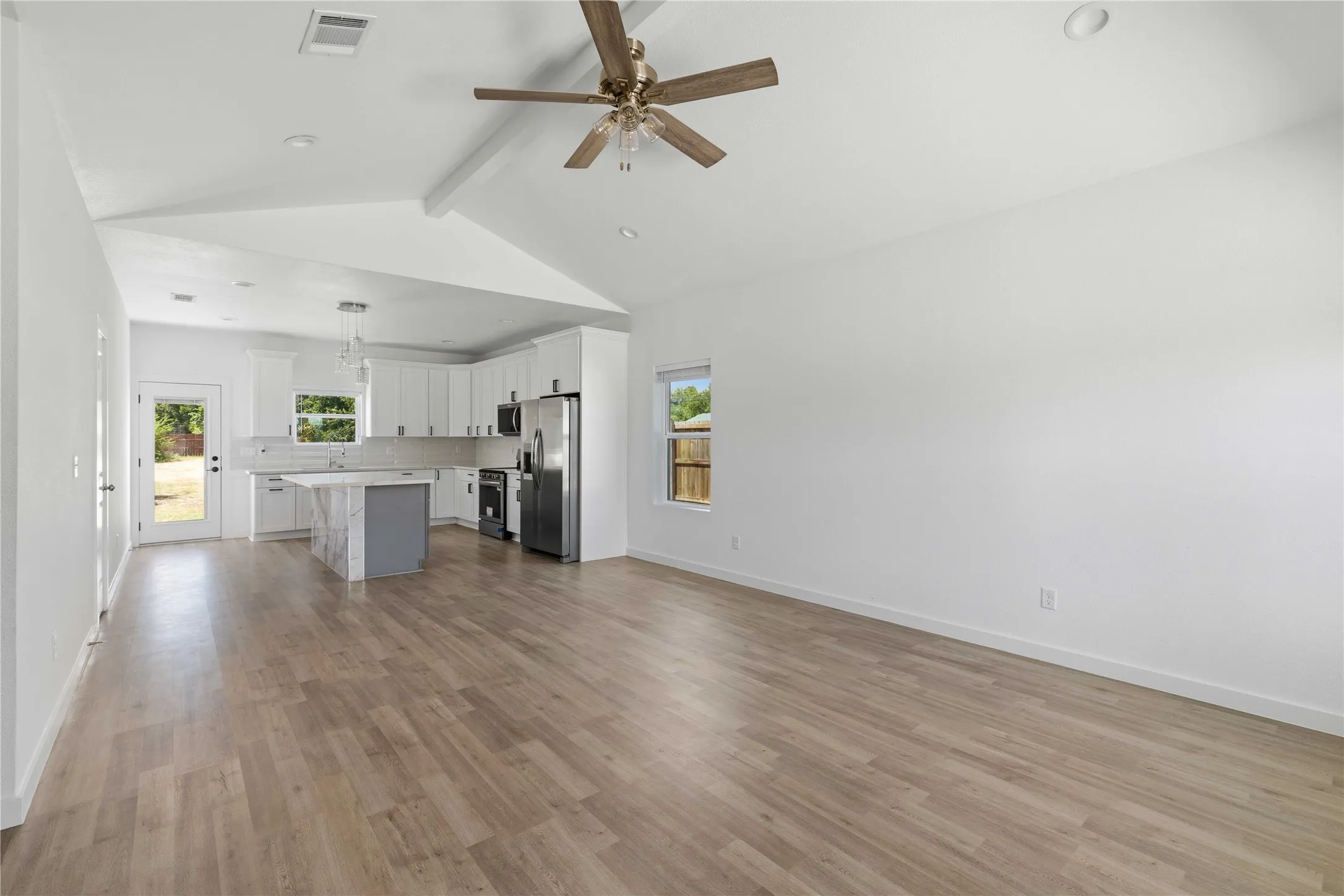 Vaulted ceiling with exposed beam, wood-finish flooring, recessed lighting, kitchen island with waterfall countertop, and stainless steel appliances