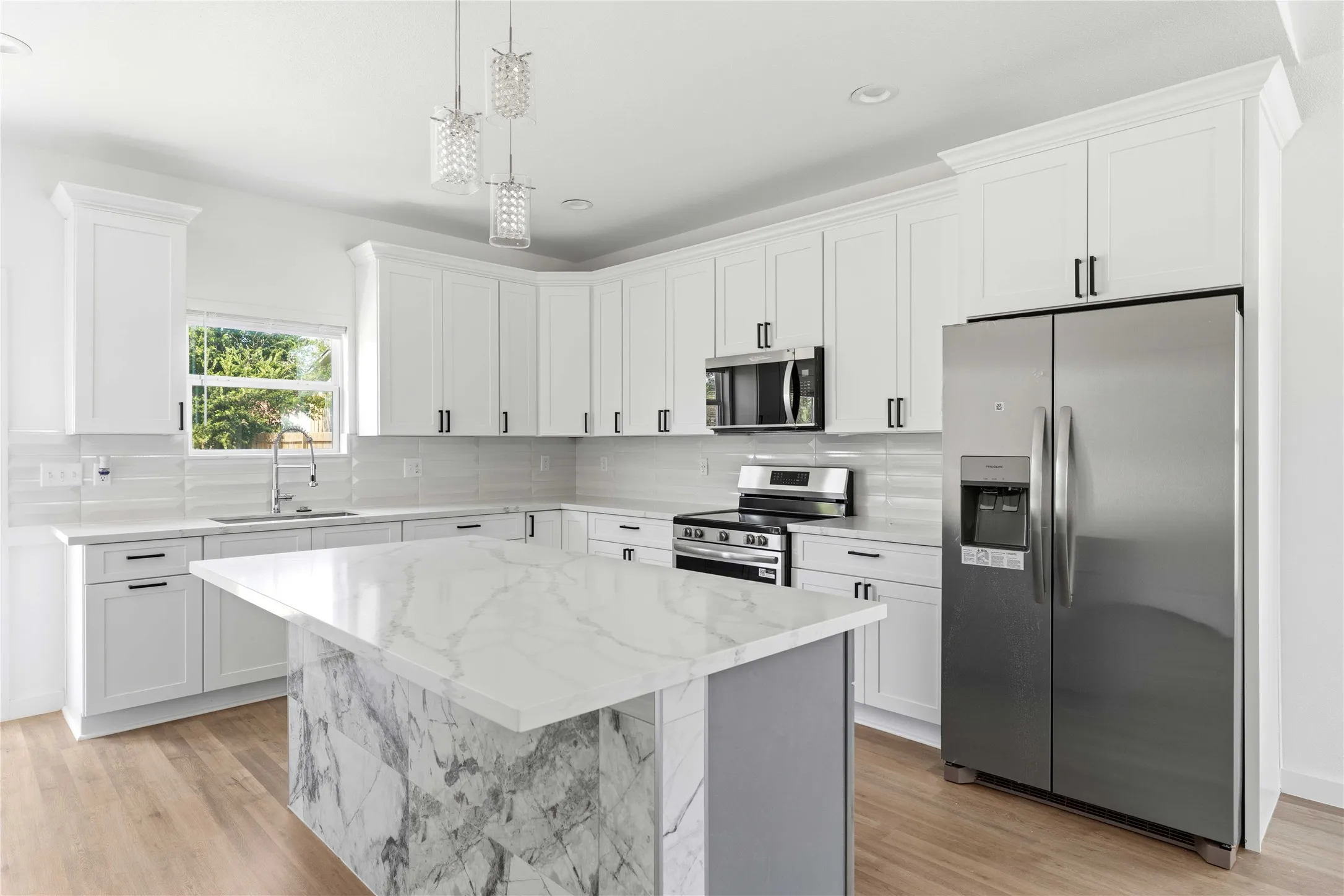 White shaker cabinetry with crown molding, stainless steel appliances, a center island with a waterfall countertop, wood-finish flooring, and pendant lighting