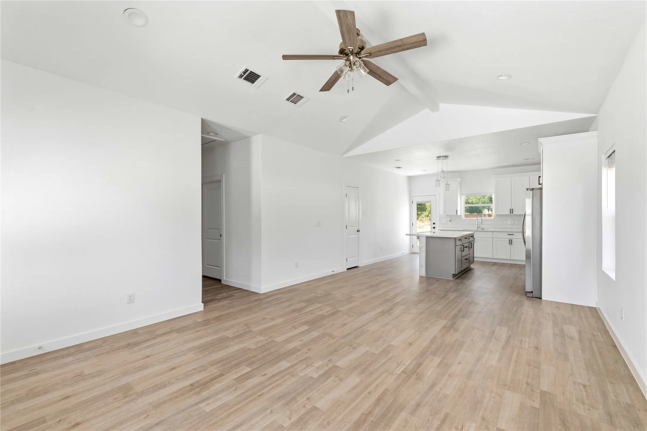 Expansive living area with wood-finish flooring, vaulted ceiling, and recessed lighting
