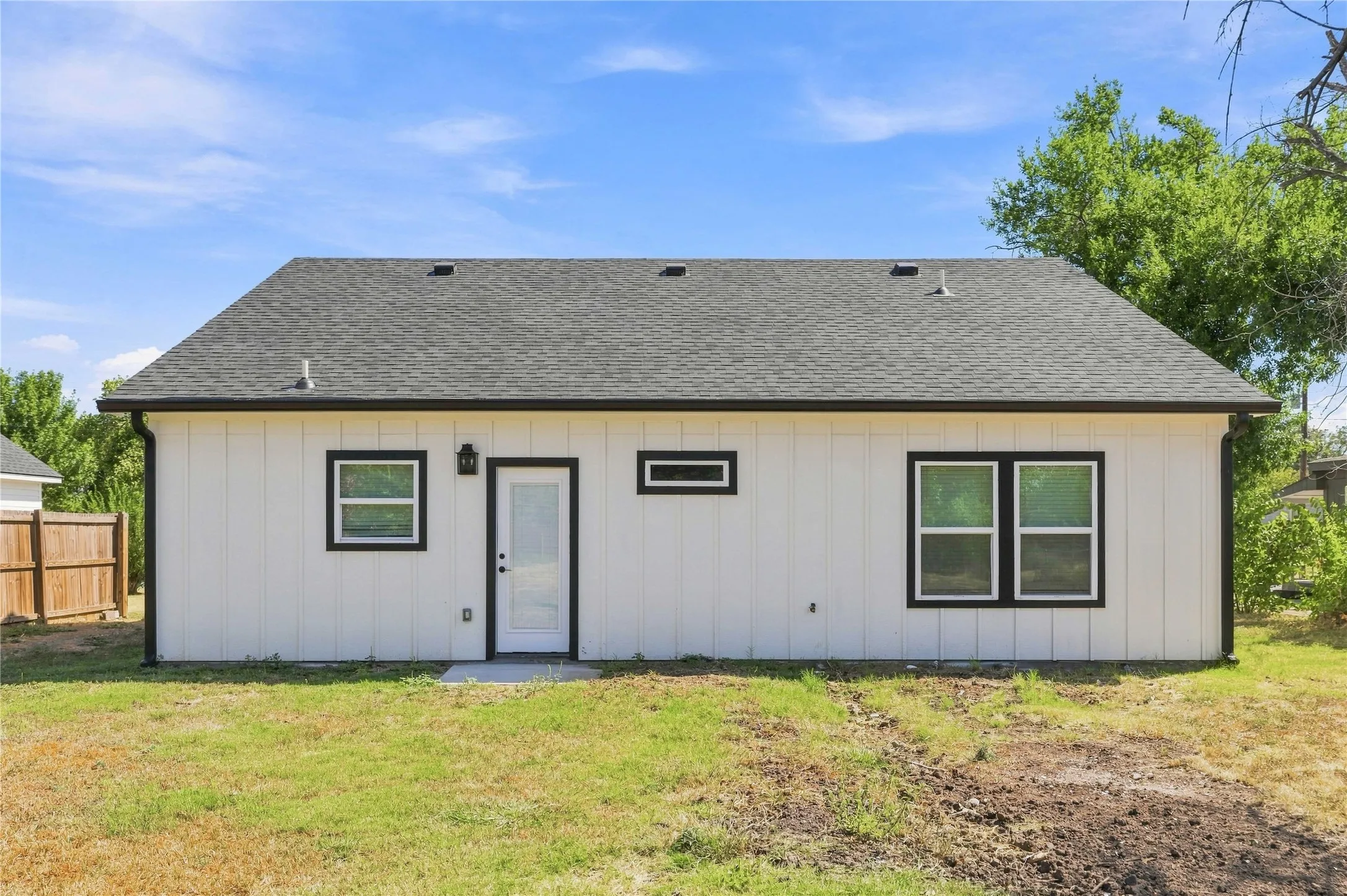 Newly constructed residence featuring a dark shingle roof, white vertical panel siding, and contrasting black-framed windows