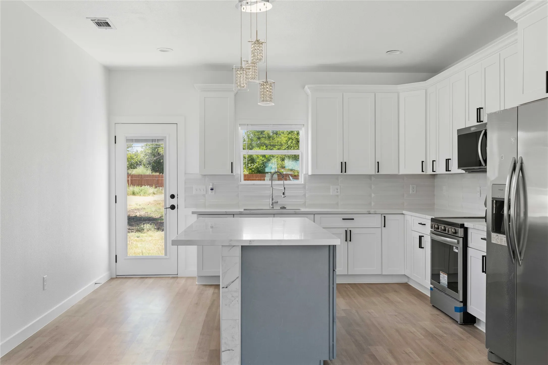 Contemporary kitchen featuring white cabinetry, light countertops, wood-finish flooring, and stainless steel appliances