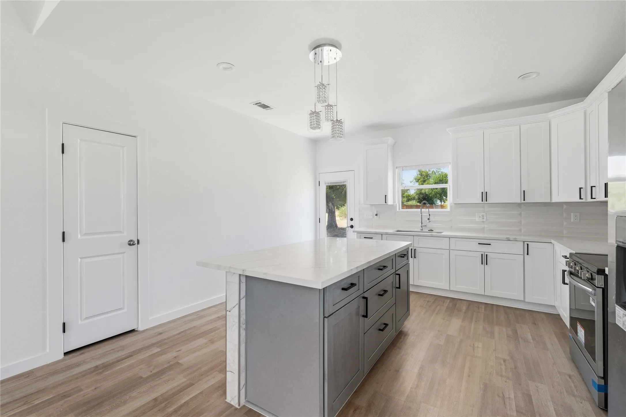 Kitchen featuring an island with built-in storage, white cabinetry, integrated appliances, wood-finish flooring, and a contemporary chandelier
