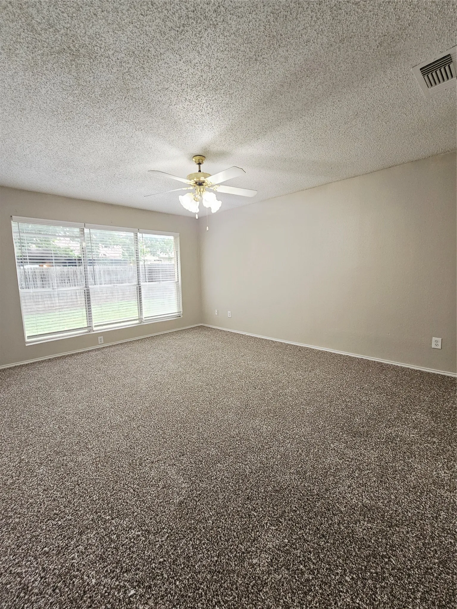 Spacious interior room featuring neutral wall paint, textured ceiling, and a ceiling fan with integrated lighting
