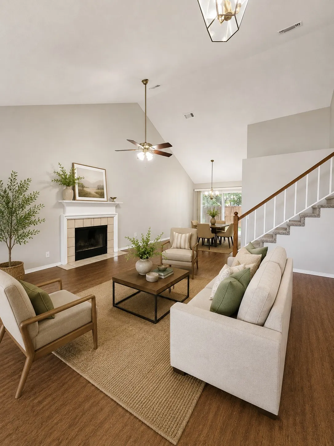 Spacious living area featuring vaulted ceilings, wood-finish flooring, a fireplace with a mantel, and a staircase with white balusters