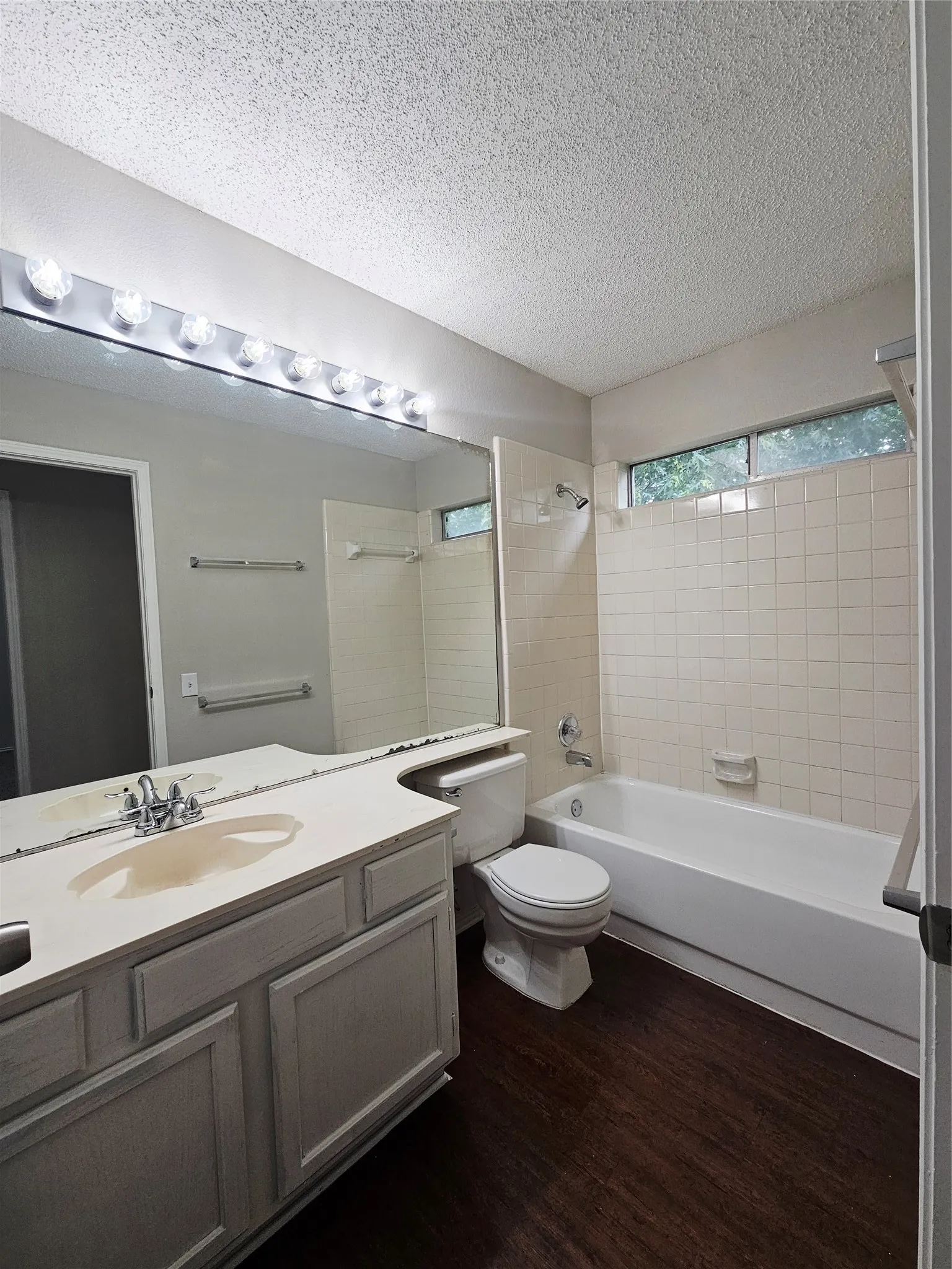 Bathroom featuring a vanity with an integrated sink, a full-width mirror, and a tub with tile surround