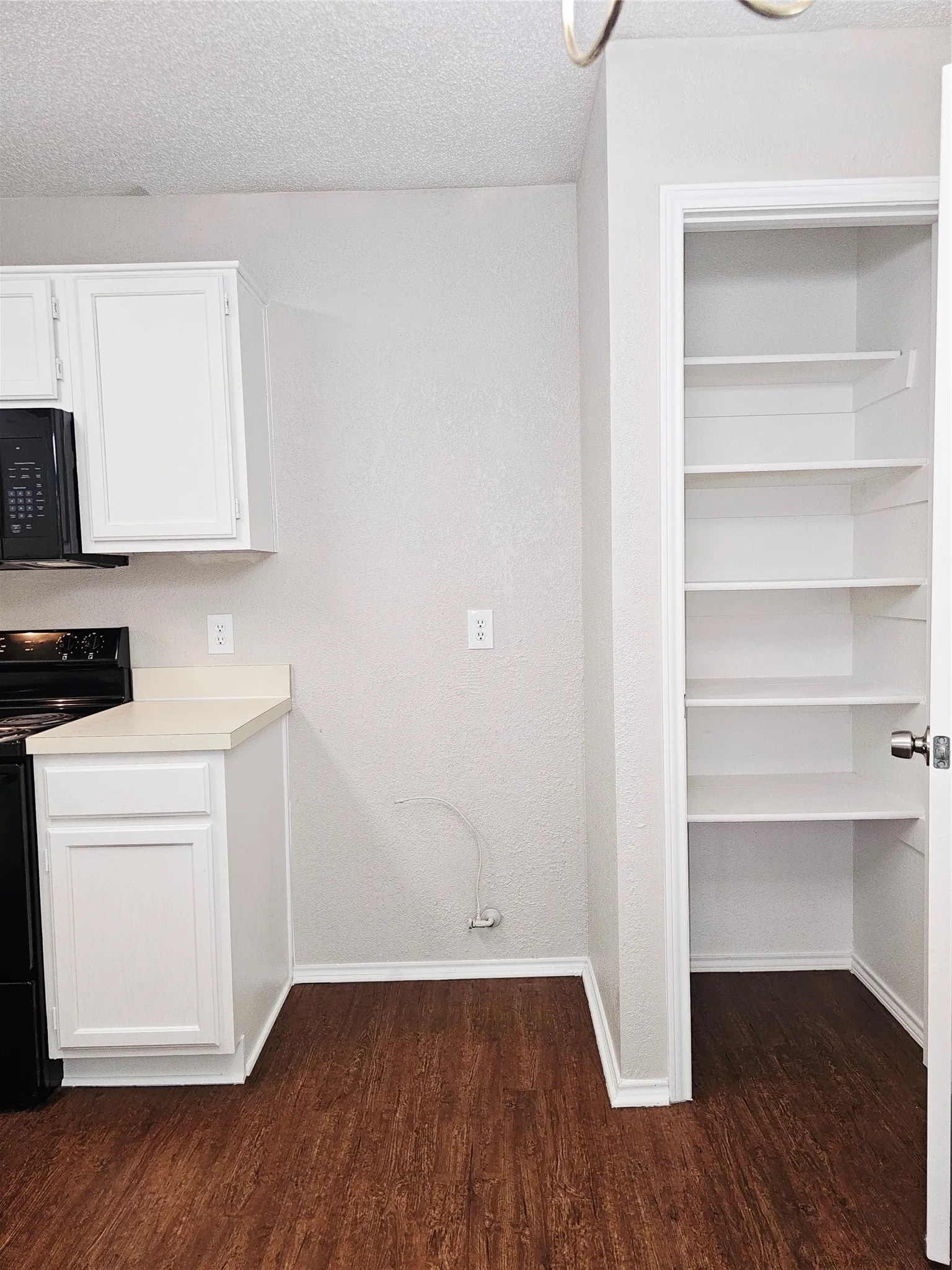 Kitchen area featuring wood-finish flooring, white cabinetry, and a pantry with multiple shelves