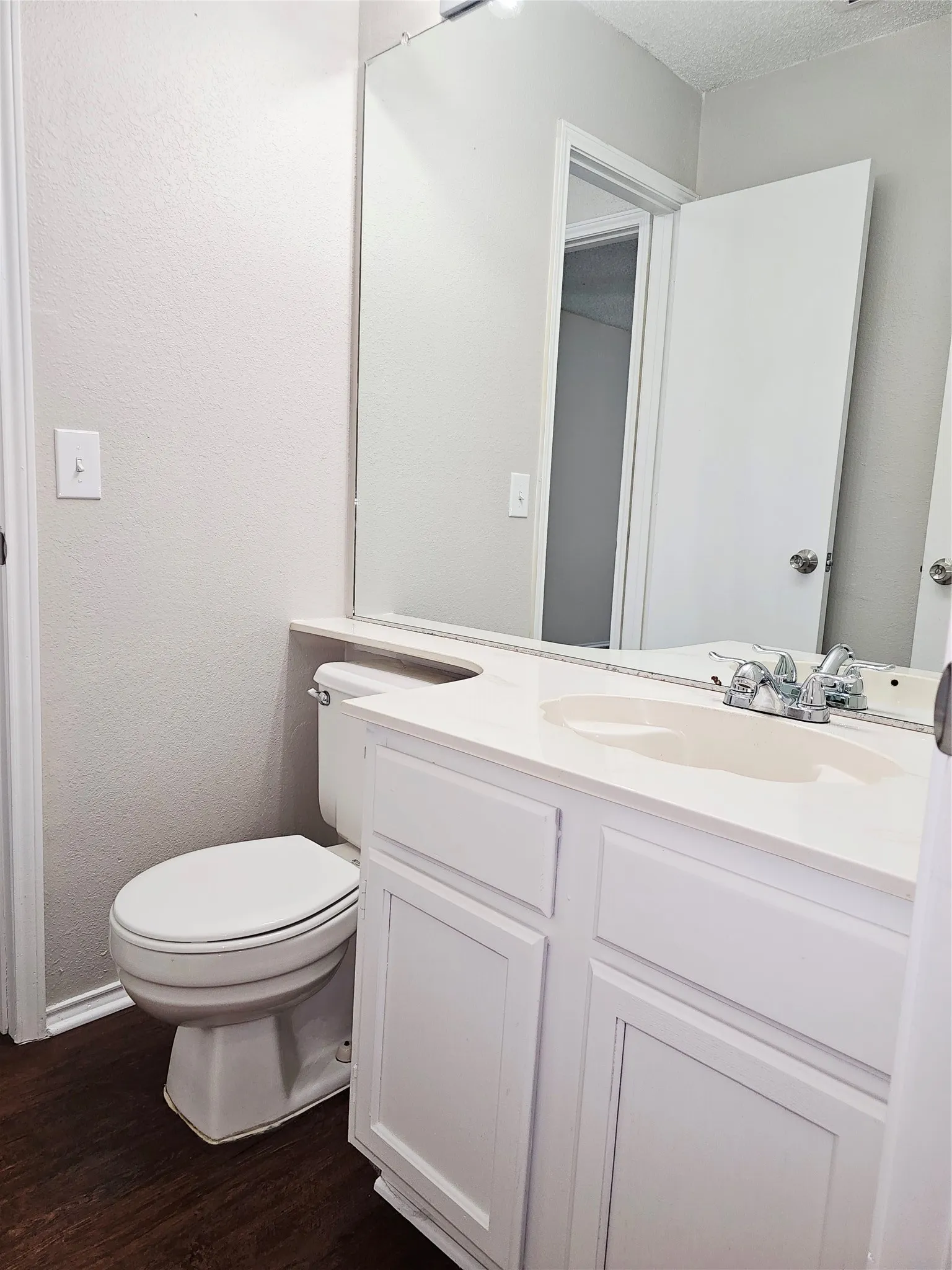 Bathroom featuring a white vanity with integrated sink, chrome faucet, wall-mounted mirror, and wood-finish flooring